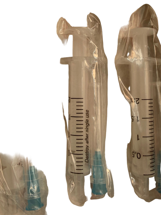 Three packaged medical syringes in clear plastic blister packs with blue needle tips, shown on a light beige surface.
