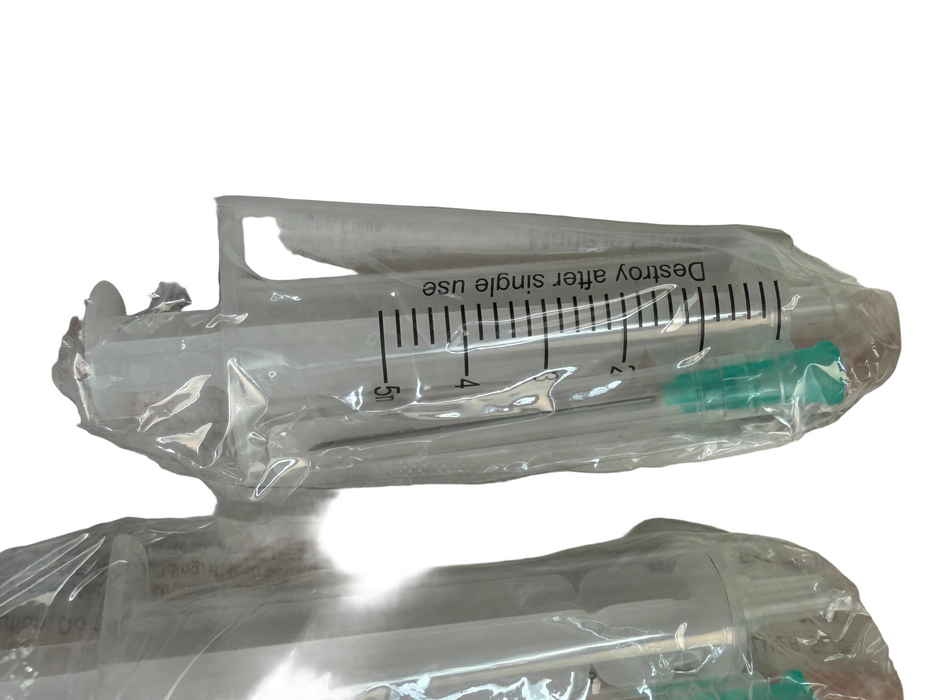Several clear plastic syringe-style applicators or transfer devices wrapped in transparent protective plastic, laid on a light fabric surface. One device in the center has printed measurement markings and the text 'Destroy after single use.